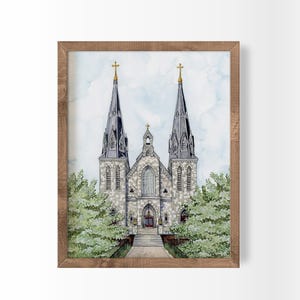 May include: Watercolor painting of a church with two tall spires topped with gold crosses. The church is framed by a light brown wooden frame and surrounded by green trees. The sky is a light blue with watercolor effects.