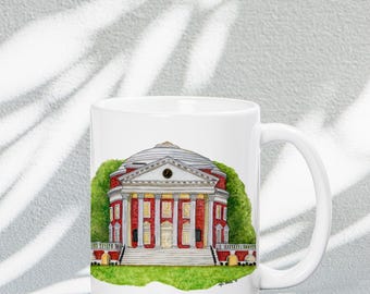 May include: White ceramic coffee mug with a red brick building with a white dome and columns. The building is surrounded by green grass and trees. The mug has a white handle.