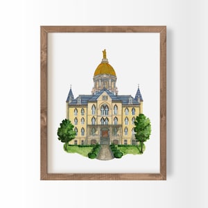 May include: Watercolor painting of a university building with a gold dome and statue, framed in a wooden frame. The building is yellow with blue roofing and green trees on either side. A path leads to the entrance.