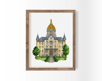 May include: Watercolor painting of a university building with a gold dome and statue, framed in a wooden frame. The building is yellow with blue roofing and green trees on either side. A path leads to the entrance.