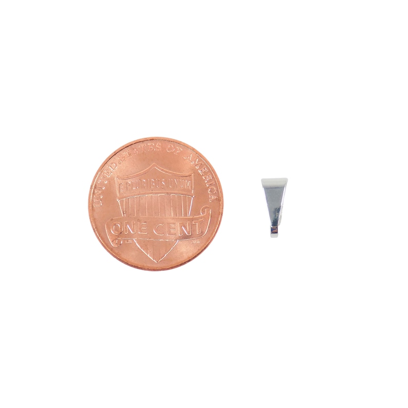 Puede incluir: Un peque&ntilde;o colgante plateado con un dise&ntilde;o triangular, junto a una moneda estadounidense de un centavo. El colgante tiene una superficie lisa y reflectante y un peque&ntilde;o lazo en la parte superior para una cadena. La moneda es de color cobre y muestra el perfil de Abraham Lincoln.