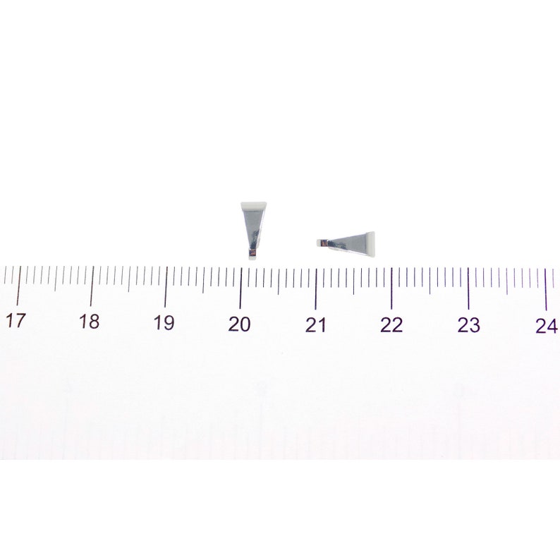 Puede incluir: Dos peque&ntilde;os hallazgos met&aacute;licos plateados con forma triangular y parte superior blanca. Los hallazgos est&aacute;n colocados sobre una superficie blanca junto a una regla, con marcas en cent&iacute;metros.