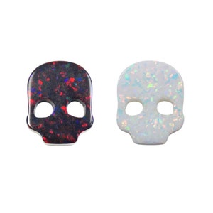 May include: Two skull-shaped opal cabochons, one black with red and blue inclusions, the other white with iridescent shimmer.