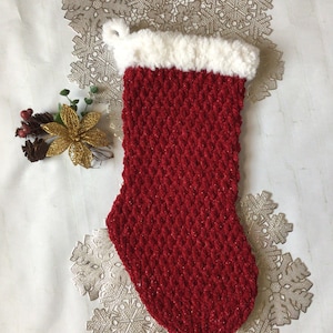 May include: Red knitted Christmas stocking with a white faux fur cuff. The stocking is decorated with a sparkly red yarn.