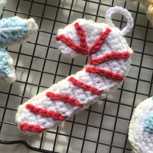 May include: A white crocheted candy cane ornament with red stripes. The ornament is hanging on a wire rack.