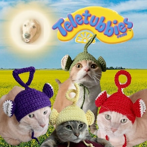 May include: Four cats wearing crocheted hats inspired by Teletubbies characters. The hats are purple, green, yellow, and red, each featuring a unique antenna shape and ear flaps. The image includes the Teletubbies logo and a dog face in the sun.