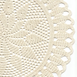 May include: A close-up of a white crocheted doily with a delicate, intricate pattern. The doily has a scalloped edge and a circular shape.