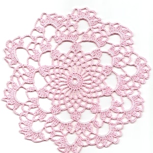 Può includere: Un delicato tovagliolo all'uncinetto rosa con un design circolare. Il tovagliolo ha un centro con un cerchio più piccolo e una serie di cerchi concentrici che si irradiano verso l'esterno.