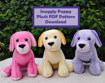 May include: Three plush puppy dogs in pink, yellow, and lavender. Each has black eyes and nose, with matching colored ears. The text "Snuggly Puppy Plush PDF Pattern Download" is in a purple box above the dogs.