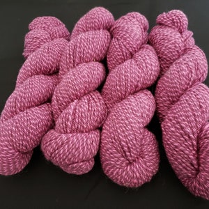 May include: Four skeins of pink yarn with a subtle shimmer. The yarn is twisted into a spiral shape.