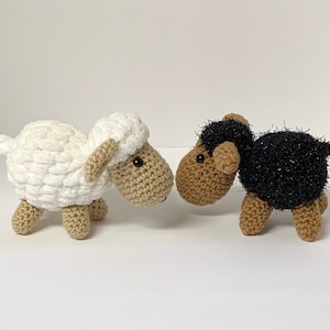 May include: Two crocheted sheep toys, one white and one black with brown faces. The sheep are facing each other.