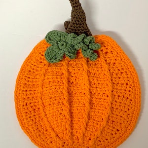 May include: A crocheted orange pumpkin with a brown stem and green leaves.