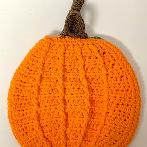 May include: A crocheted pumpkin with a brown stem and orange body. The pumpkin is made with a cable stitch pattern.