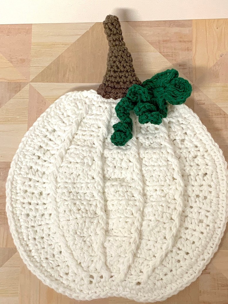 May include: White crocheted pumpkin with a brown stem and green crocheted leaves.