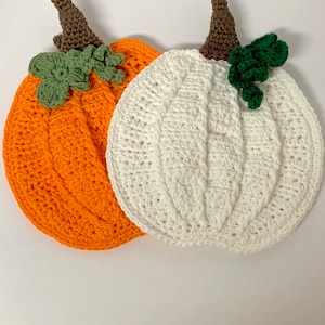 May include: Two crocheted pumpkins, one orange and one white, with green crocheted leaves on top.