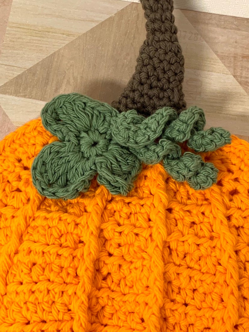 May include: A crocheted pumpkin decoration with a brown stem and green leaves. The pumpkin is orange and has a textured surface.