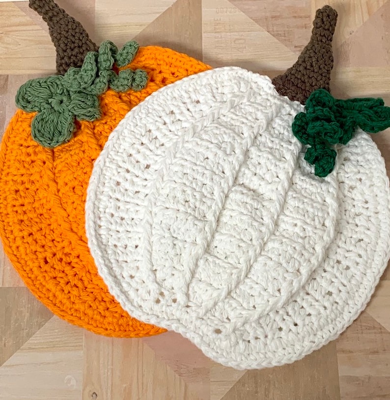 May include: Two crocheted pumpkins, one orange and one white, with green crocheted stems.