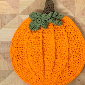 May include: A crocheted pumpkin with a brown stem and green leaves. The pumpkin is orange and has a textured surface.