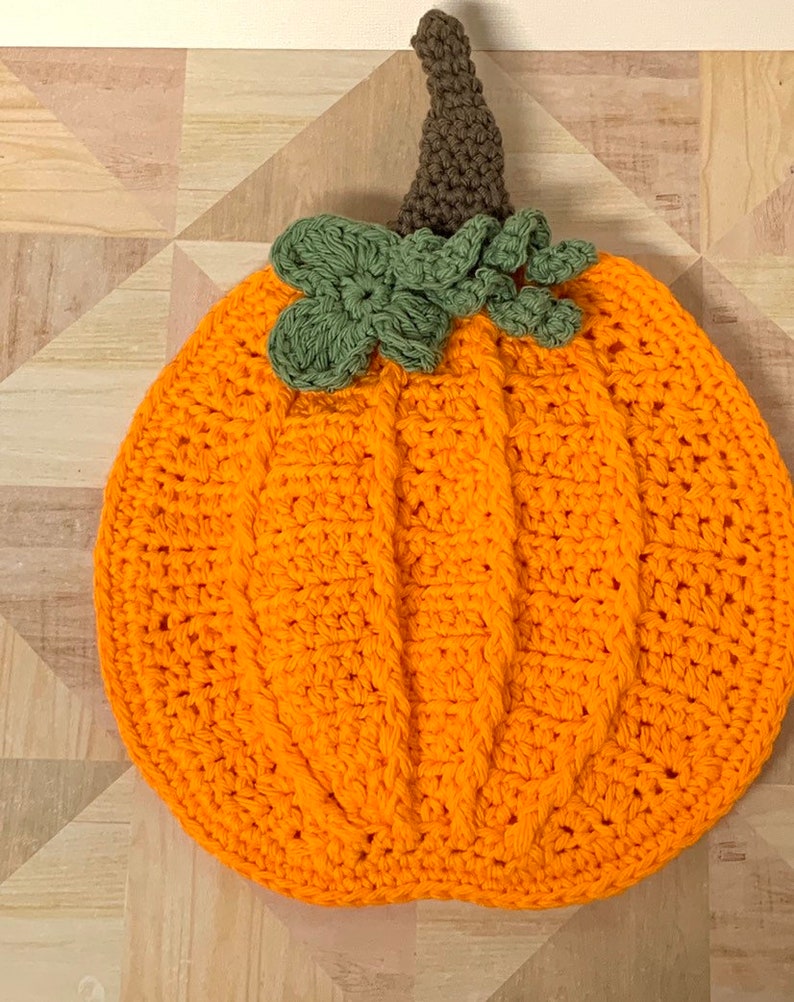 May include: A crocheted pumpkin with a brown stem and green leaves. The pumpkin is orange and has a textured surface.