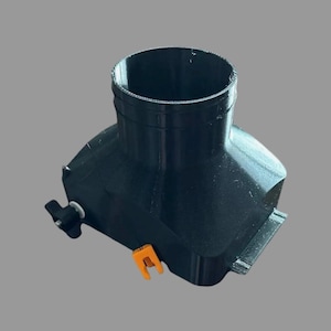 May include: A black plastic component with a cylindrical opening at the top and a rectangular base. It features an orange clip and a black knob. The object is designed for a specific mechanical or industrial application.