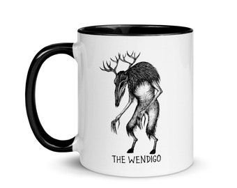 May include: White ceramic coffee mug with a black rim and handle. The mug features a black and white illustration of a creature with antlers and the text "THE WENDIGO".