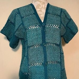 May include: A teal blue crocheted cardigan with a button-up front and a square pattern.