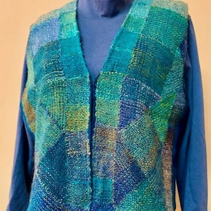 Könnte beinhalten: Eine gewebte Weste in Teal, Blau und Grün mit Reißverschluss. Die Weste ist aus einem strukturierten Stoff gefertigt und hat ein geometrisches Muster.