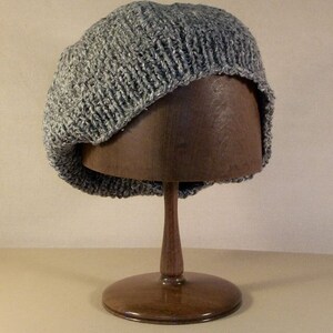 May include: A grey knitted beanie with a slouchy fit, displayed on a wooden hat stand.