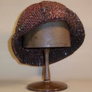 May include: A brown and white knitted hat with a slouchy design. The hat is displayed on a wooden hat stand.