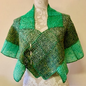 Puede incluir: Un chal tejido en verde y blanco con cuello de chal. El chal está hecho de un hilo suave y texturizado y tiene un sutil efecto degradado.