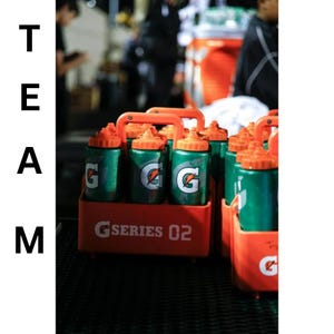 Pode incluir: Um conjunto de garrafas de &aacute;gua desportivas de pl&aacute;stico verde com tampas cor de laranja, cada uma com um log&oacute;tipo G branco, mantidas num suporte de pl&aacute;stico cor de laranja com pega. O suporte tem a etiqueta G SERIES 02. O texto vertical TEAM &eacute; vis&iacute;vel.
