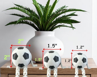 May include: Three soccer ball figurines with articulated legs and arms, labeled L (2" x 2"), M (1.5" x 1.5"), and S (1.2" x 1.2"). The balls are white with black pentagon shapes. The text "SIZE OPTIONS" is at the top.