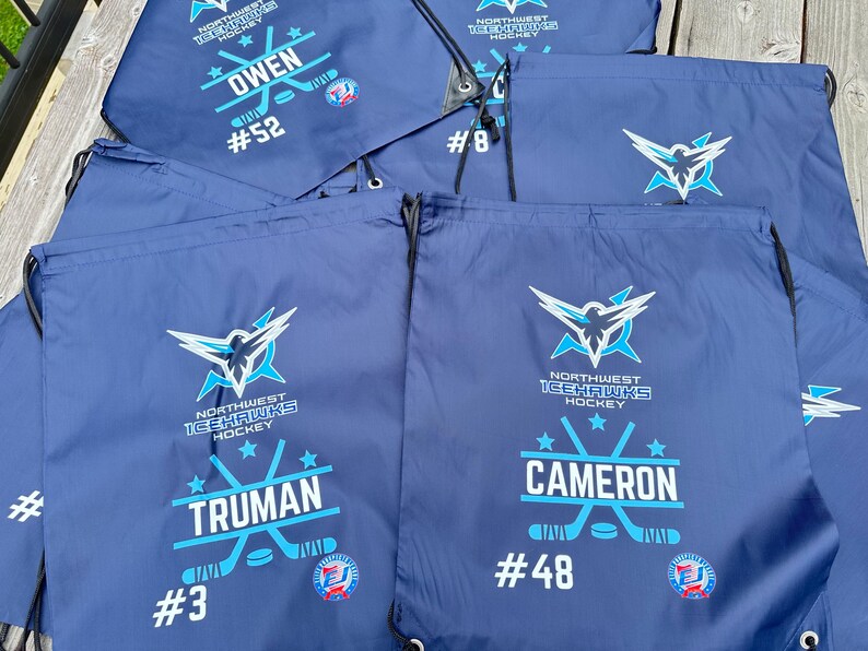 May include: A collection of navy blue drawstring bags featuring the Northwest Icehawks Hockey logo in light blue and white. Each bag is personalized with a player's name, such as Owen, Truman, or Cameron, along with their specific jersey number.