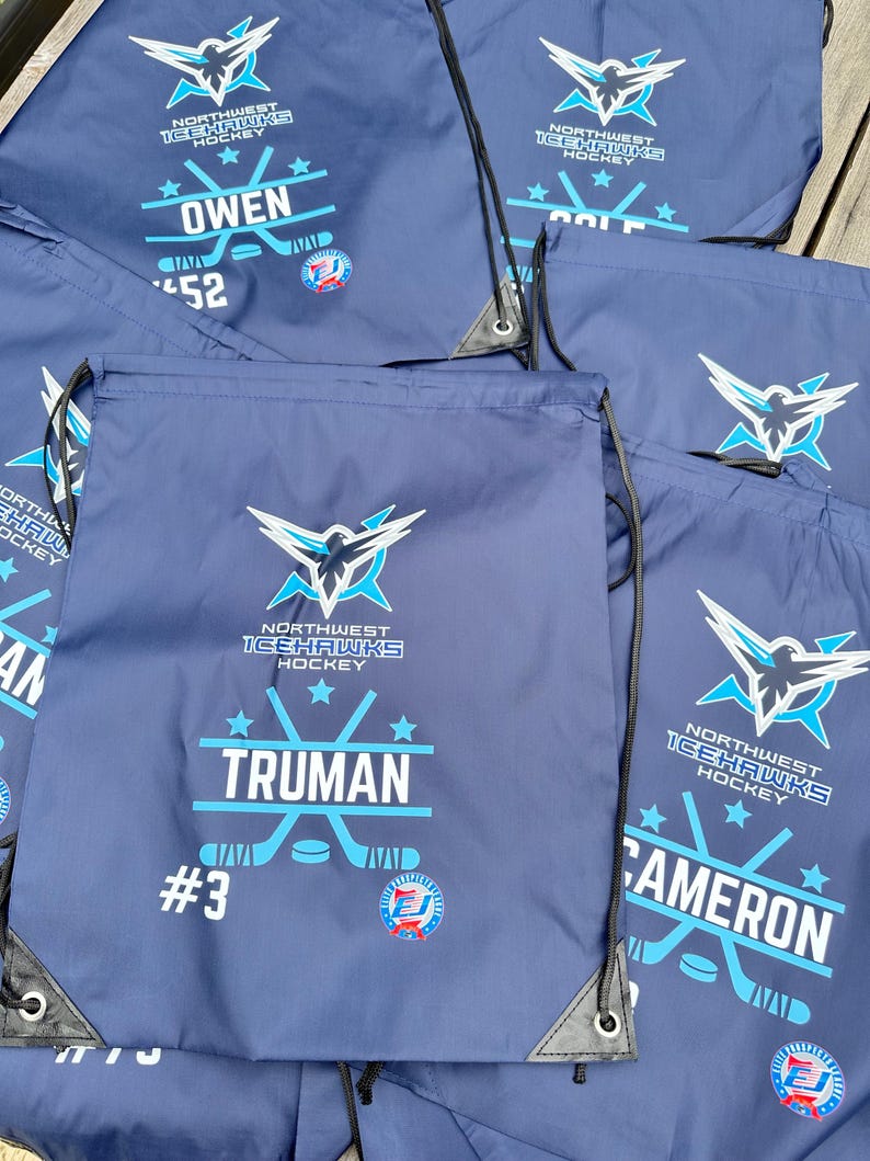 May include: A collection of navy blue drawstring bags featuring the Northwest Icehawks Hockey logo in white and light blue. Each bag is personalized with a player's name, such as Truman, Owen, or Cameron, along with a jersey number and a hockey graphic.