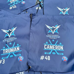 May include: A collection of navy blue drawstring bags featuring the Northwest Icehawks Hockey logo in white and light blue. Each bag is personalized with a player's name, such as Truman or Cameron, and a jersey number like #3 or #48.