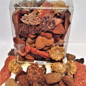 May include: A clear plastic container filled with a variety of dog treats. The treats are in different shapes, sizes, and colors, including brown, orange, and yellow. The container has a label that says "BEST BY: 02/29/23".