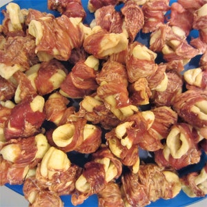 May include: A close-up of a bowl filled with dog treats. The treats are made of dried meat and are shaped like knots. The treats are a light brown color and have a slightly chewy texture.