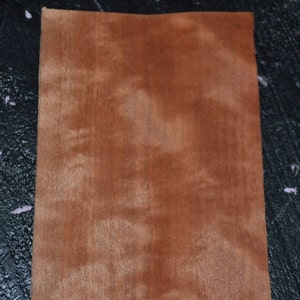 May include: A close-up of a piece of wood veneer with a reddish-brown color and a natural wood grain pattern.