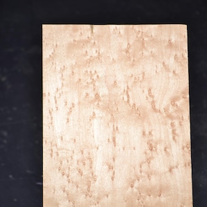 May include: A rectangular piece of light-colored wood with a unique, speckled pattern. The wood grain features small, dark spots and swirls, creating a natural, textured appearance. The wood is likely for woodworking or craft projects.