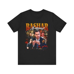 May include: Black t-shirt featuring a graphic of Bashar Al-Assad with the text "Bashar Al-Assad" in orange and white. The graphic includes multiple images of the person against a cityscape background.