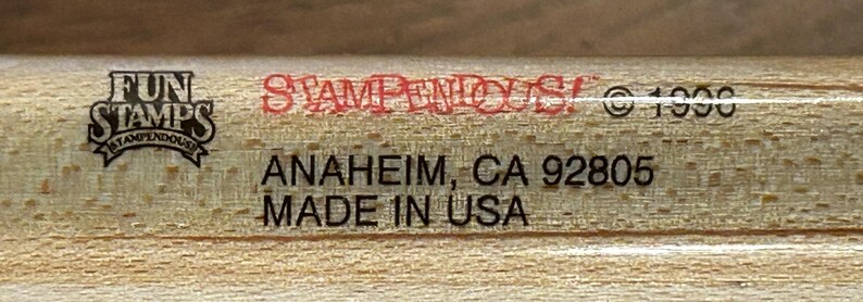 May include: Close-up of a wooden stamp with the text "FUN STAMPS STAMPENDOUS" in a black and white logo. The text "STAMPENDOUS" is in red. Below is "ANAHEIM, CA 92805 MADE IN USA" in black text. The copyright symbol and the year 1996 are also visible.