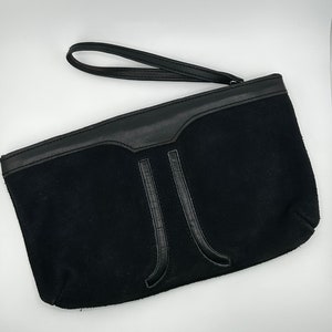 Può includere: Una pochette in pelle scamosciata nera con manico in pelle e un design a forma di J in pelle.