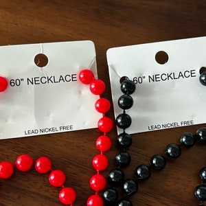 Puede incluir: Dos collares de 152 cm, uno rojo y otro negro, en tarjetas blancas con el texto "60" NECKLACE" y "LEAD NICKEL FREE".
