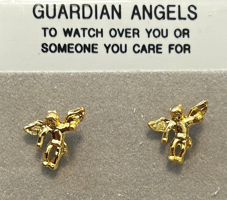 Pode incluir: Um par de brincos dourados com um pequeno design de anjo. Os brincos s&atilde;o embalados em um cart&atilde;o branco com o texto "Guardian Angels To Watch Over You Or Someone You Care For".