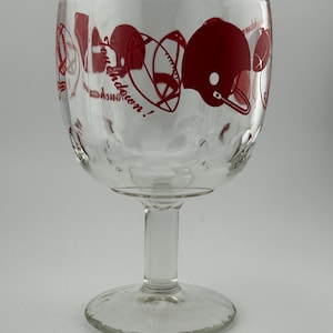 May include: Clear glass goblet with a wide bowl and a stem. The goblet is decorated with red football helmets, footballs, and the words "Touchdown!" around the rim. The glass has a textured surface.