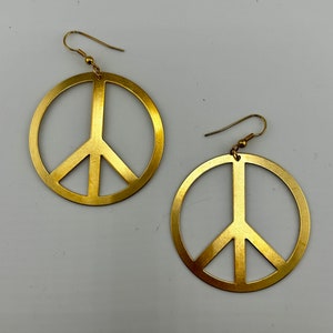 May include: A pair of gold peace sign earrings. The earrings are made of metal and have a simple, classic design.