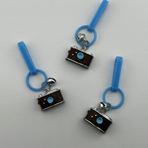 May include: Three blue plastic zipper pulls with silver camera charms. Each charm has a blue lens and a silver bell.