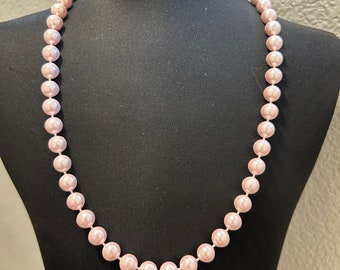 May include: A long strand of blush pink faux pearl beads on a black mannequin.