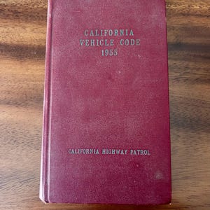 May include: A burgundy hardcover book titled "California Vehicle Code 1955" with the words "California Highway Patrol" printed on the bottom.