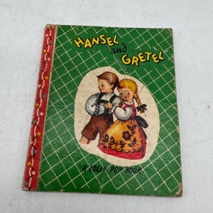 May include: Vintage children's book titled "Hansel and Gretel." The cover is green with a diamond pattern and features an illustration of the two characters. The spine has a red and white decorative design. The text "A Lolly Pop Book" is at the bottom.